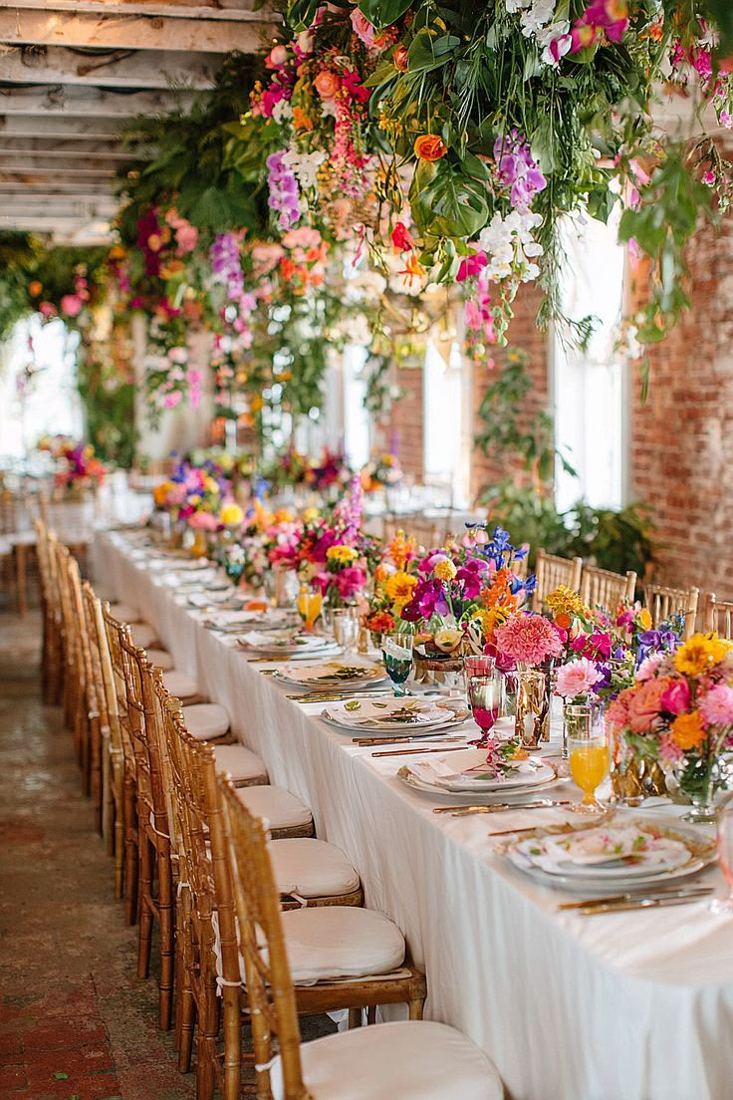 Mesa larga con camino floral bajo los arcos de la hacienda